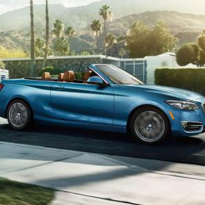 The BMW 230i Convertible in Seaside Blue Metallic cruises through the streets with the top down.