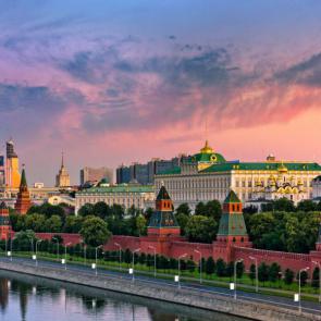 Moskva River along the Kremlin wall in Moscow, Russia, with water and a walkway in the foreground and a beautiful sunset sky in the background